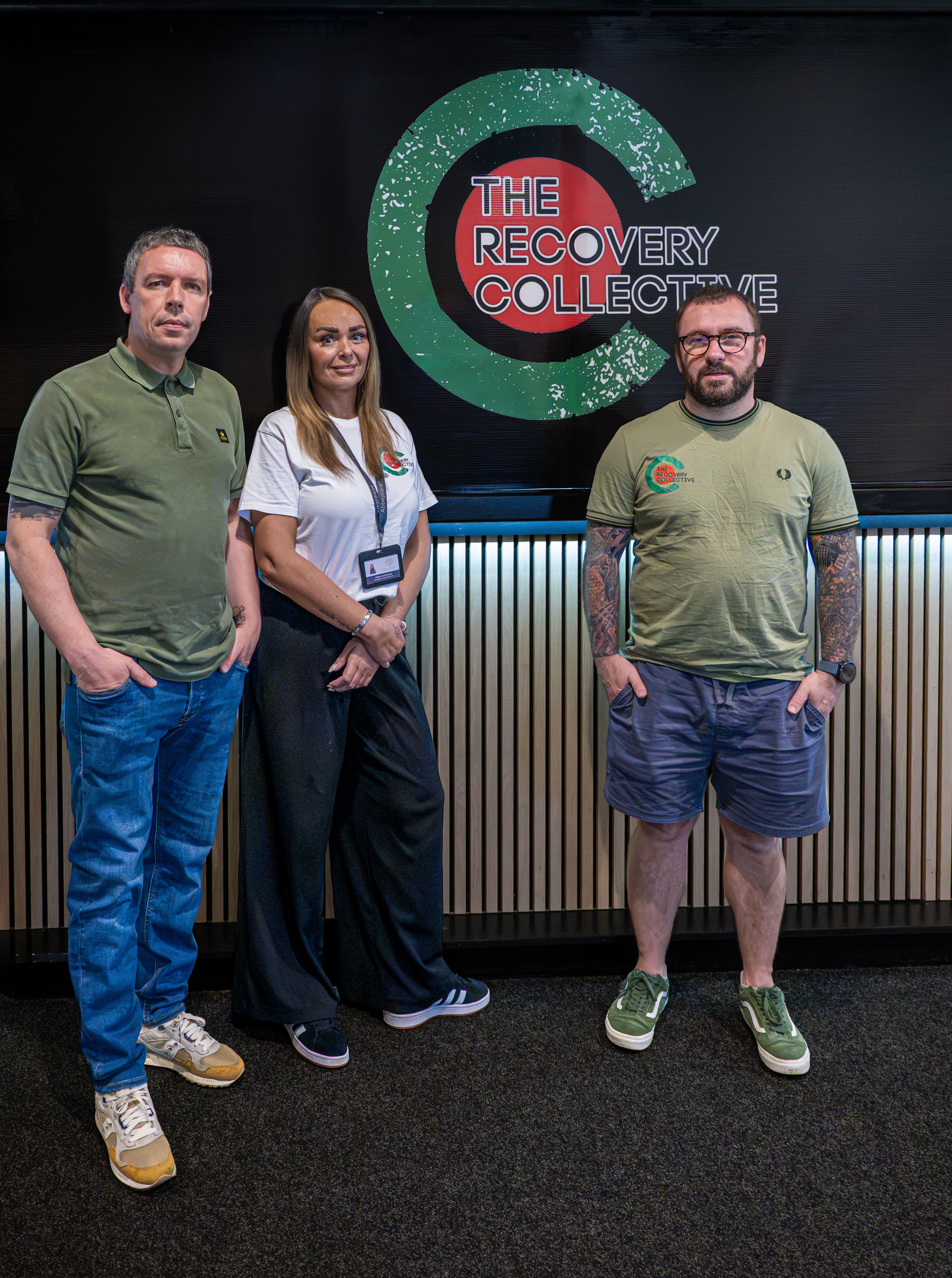 Three people standing beside The Recovery Collective banner